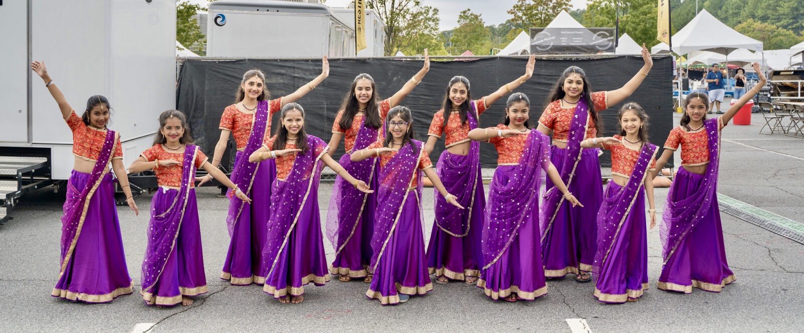 A group of girls wearing purple and red saris smile and pose.