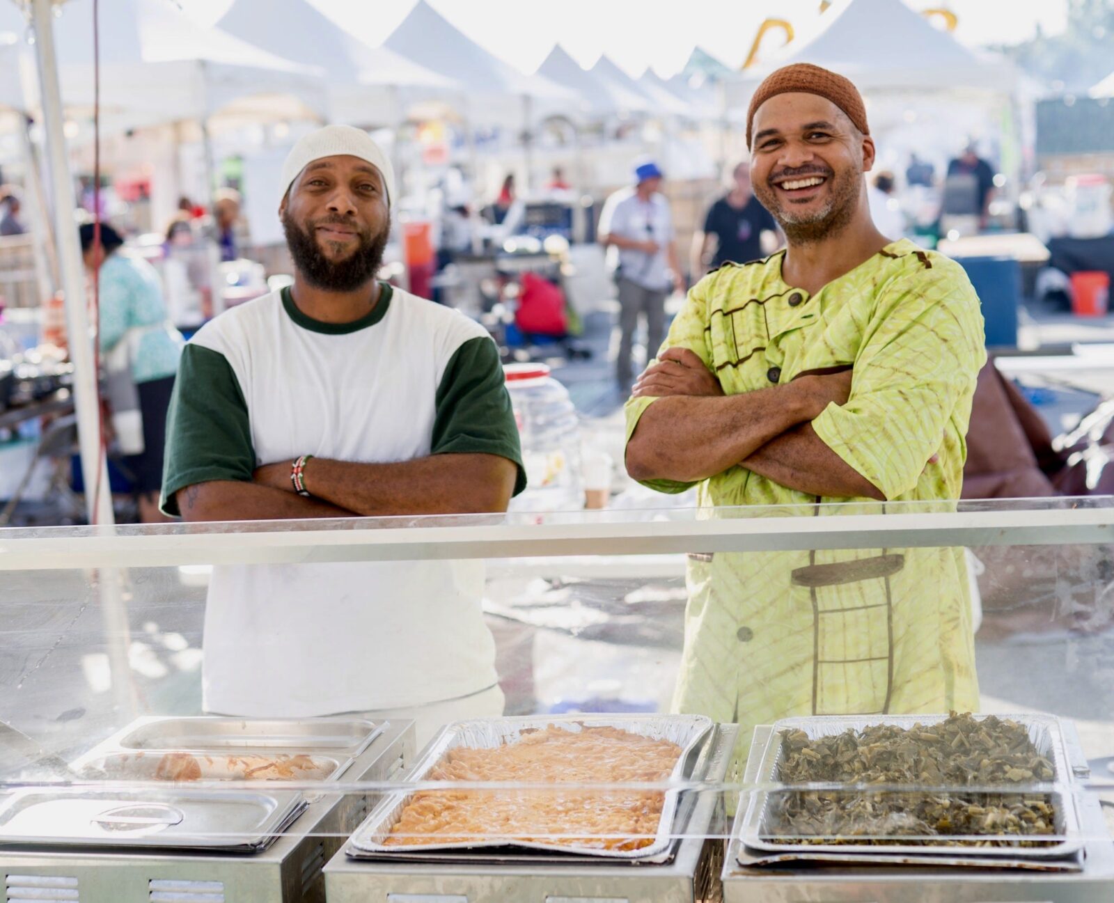 Two men are smiling standing behind the food they prepared